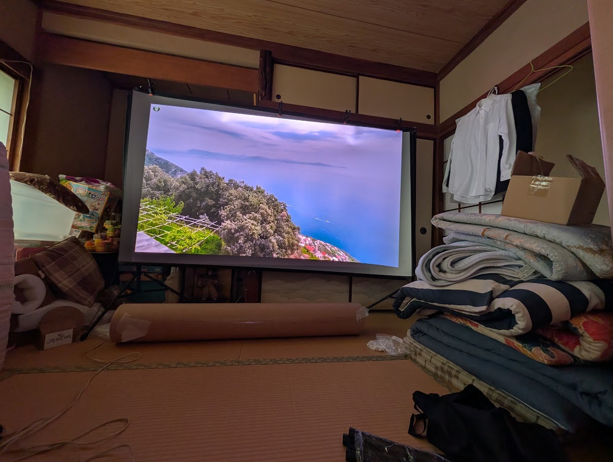 布団や荷物が置かれた8畳の和室にスクリーンを設置した様子